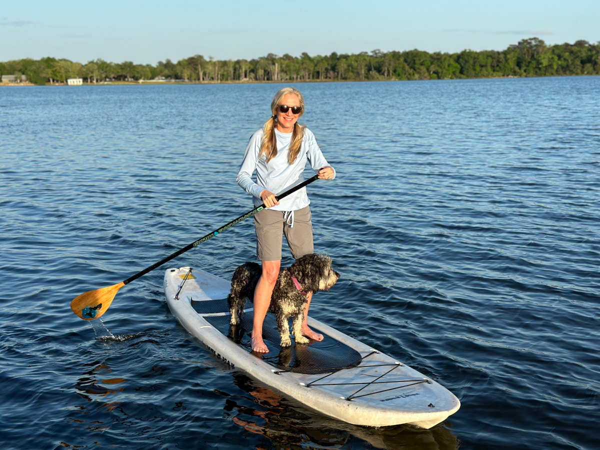 Laurie Hood paddling on a board SUP with a dog on a lake.