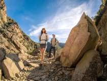 KUHL summer hiking clothing for men and women show by a man and a woman hiking on a rocky trail