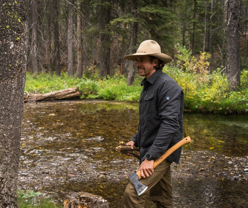 Bearanoid article image - A man holding an axe in a forest creek, wearing KUHL mens clothing.