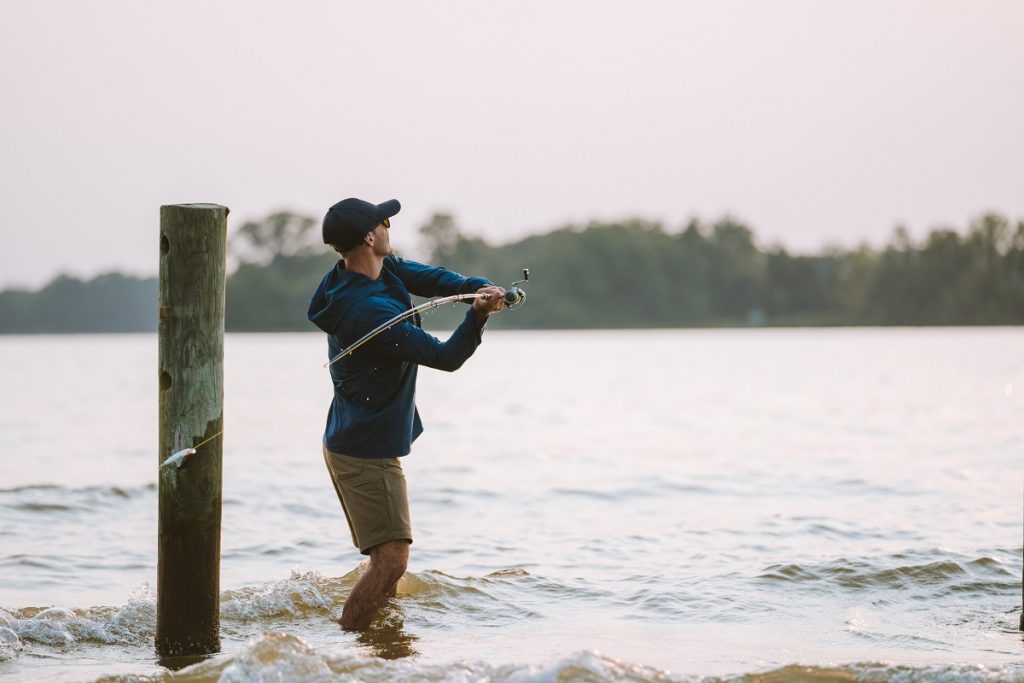 man in K&Uuml;HL clothing casting fishing lure into lake