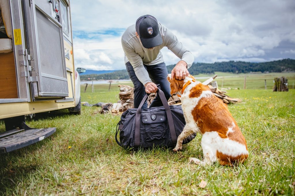 man in K&Uuml;HL cap holding K&Uuml;HL bag petting white and orange dog