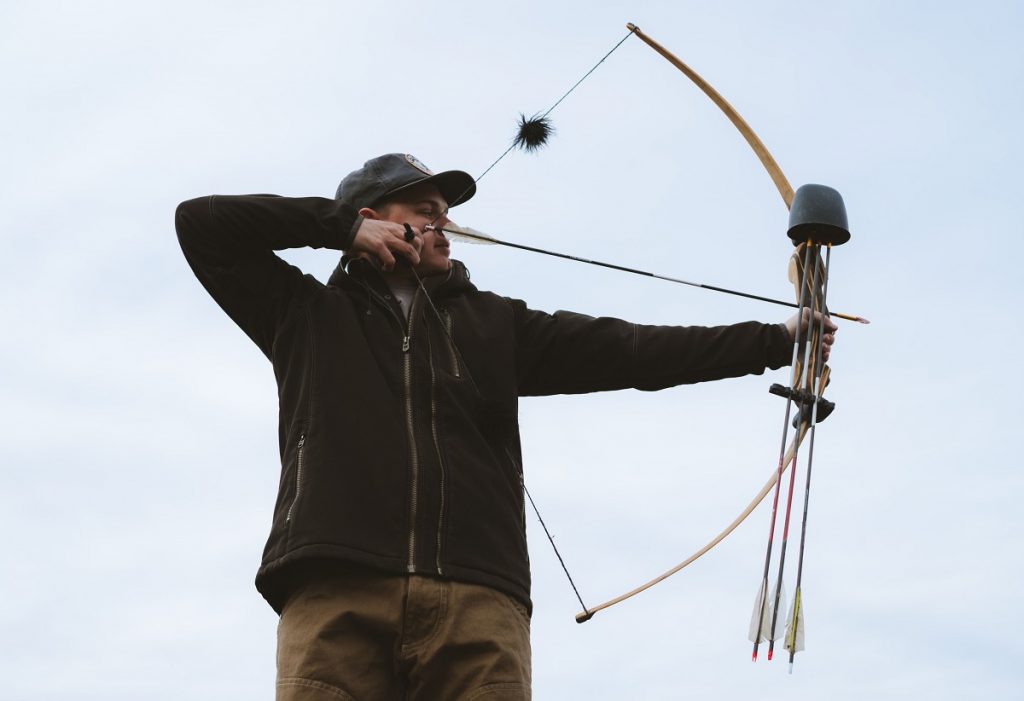 man in K&Uuml;HL jacket and K&Uuml;HL pants aiming with bow and arrow