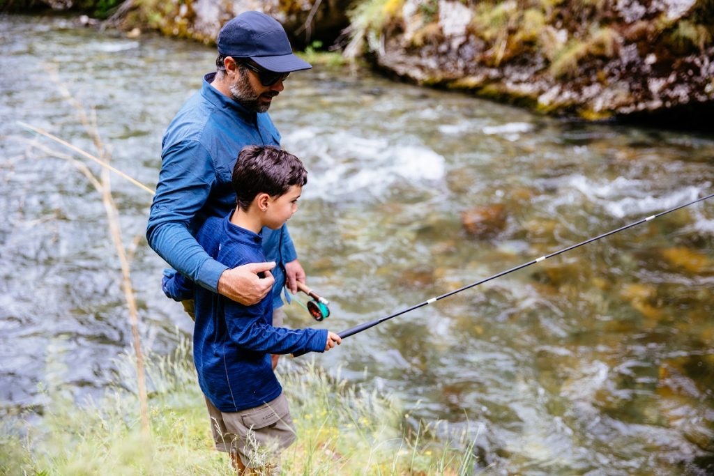 man in K&Uuml;HL shirt and K&Uuml;HL hat fishing with his son next to river