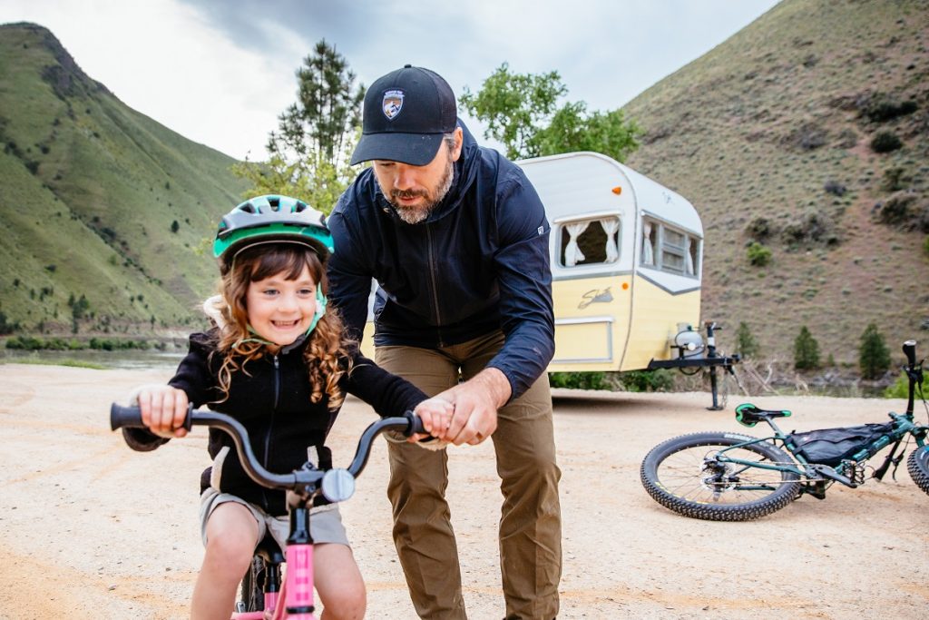 man in K&Uuml;HL clothing holding daughter on bicycle