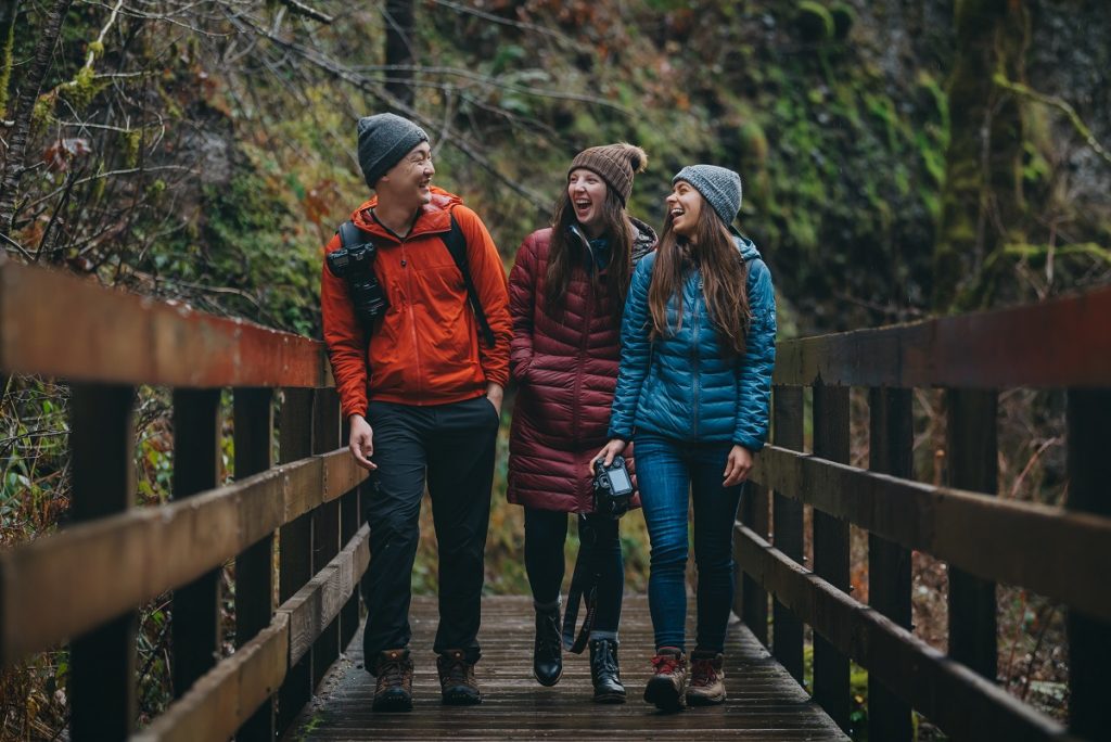 man and two women in K&Uuml;HL jacket smiling while walking on brown bridge