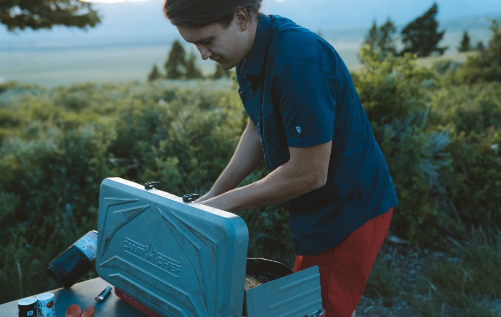 man in K&Uuml;HL short sleeve shirt cooking on portable stove
