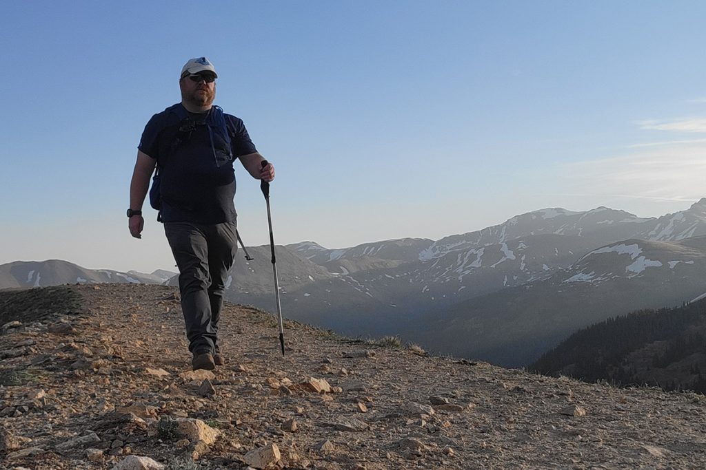 man in K&Uuml;HL pants and shirt hiking with a trekking pole during daytime
