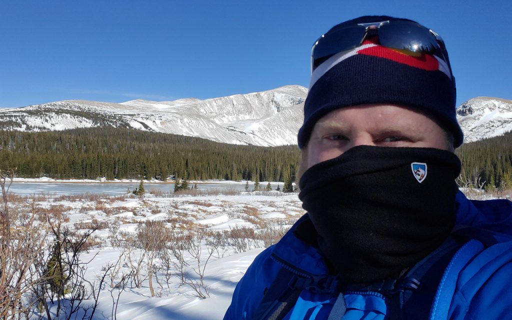 man wearing K&Uuml;HL neck gaiter facing camera on snowy field during daytime