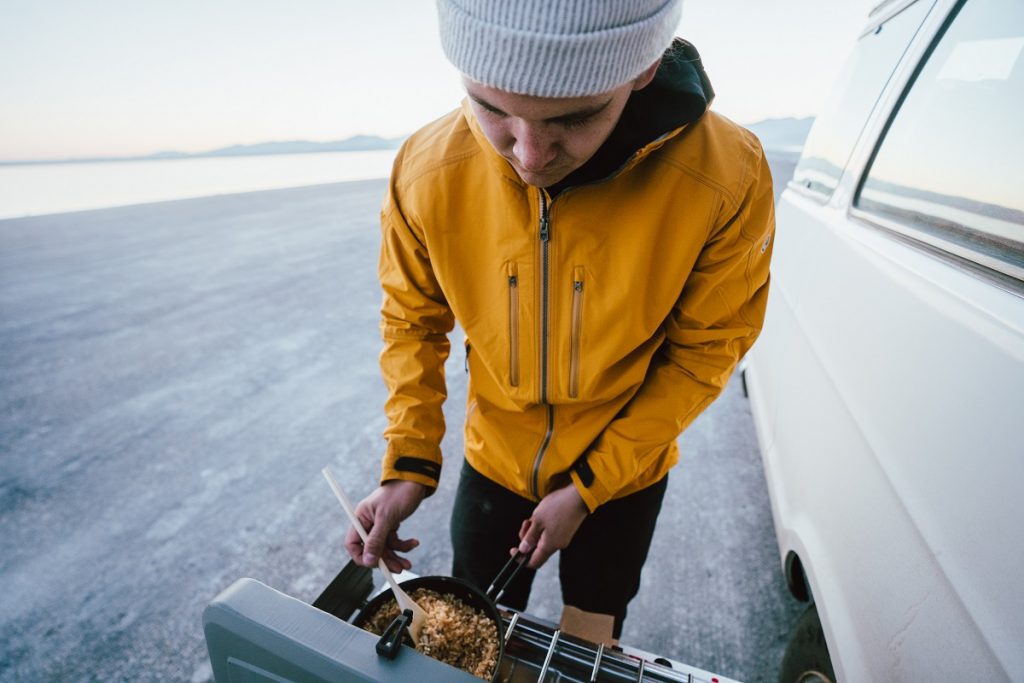 man in yellow K&Uuml;HL jacket preparing oatmeal outdoors